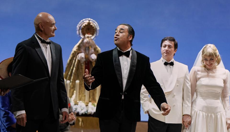 Deux hommes chantent en costume noir. Un couple de mariés au second plan