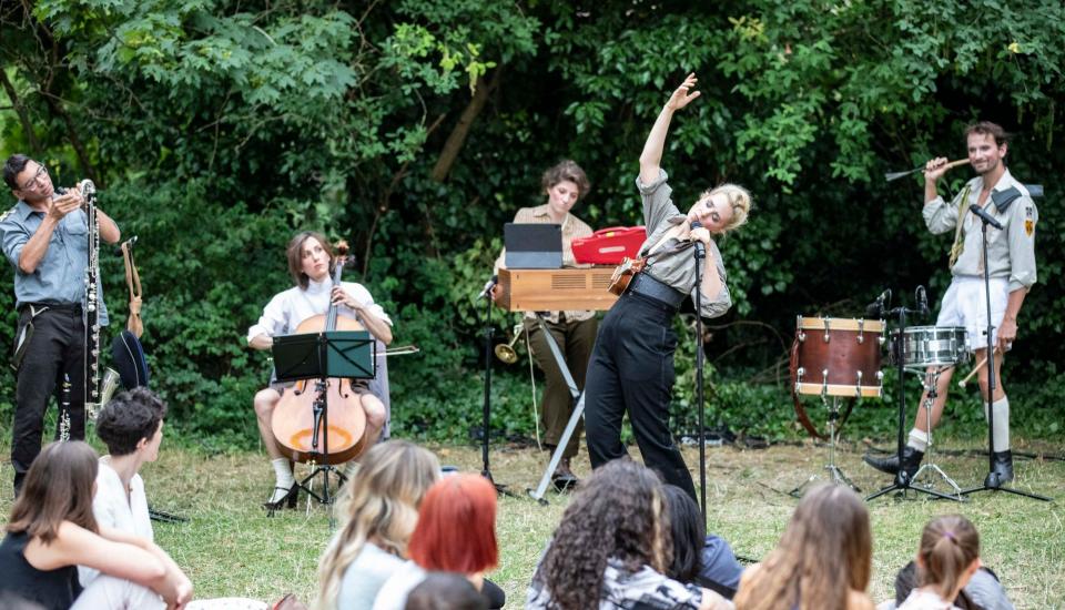 Femme chantant devant une foule, petit orchestre au second plan