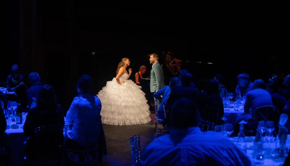 Perrine Madoeuf et Fabien Hyon chantant au sein des convives. Perrine Madoeuf porte une robe de mariée.