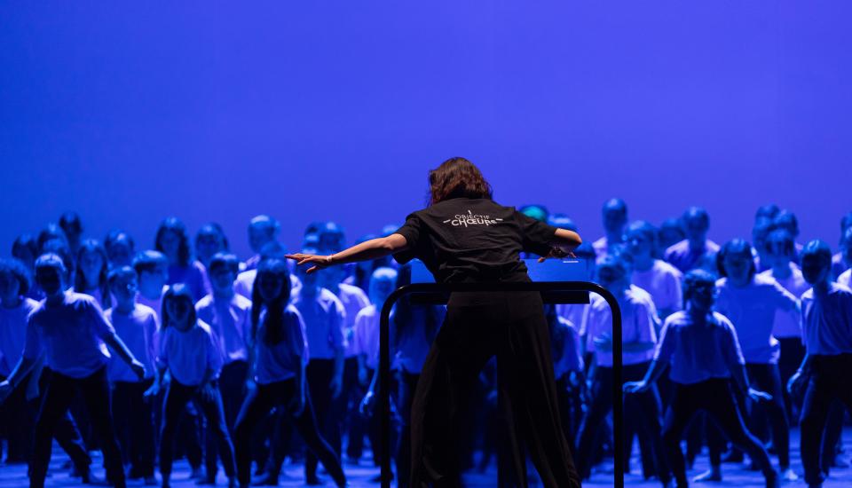 Au Chœur de l'Océan Une cheffe de chœur vue de dos, animant un chœur d'enfant.